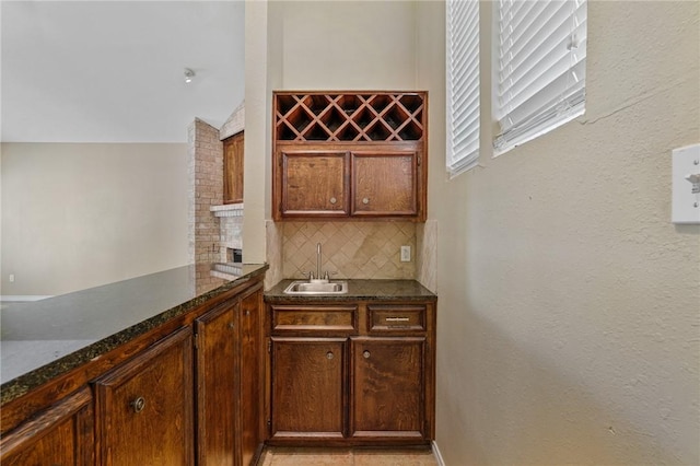 bar with backsplash, dark stone counters, and sink