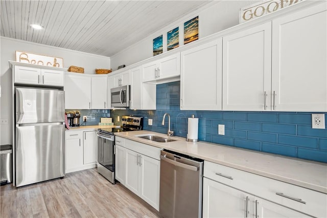 kitchen with stainless steel appliances, a sink, white cabinets, light countertops, and decorative backsplash