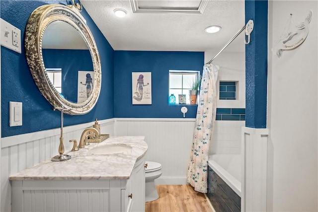 full bath featuring a wainscoted wall, a textured ceiling, wood finished floors, and toilet