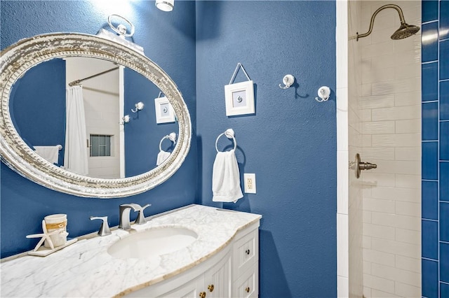 bathroom with a textured wall, a tile shower, and vanity