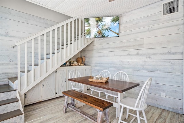 dining room with stairway, light wood-type flooring, visible vents, and wooden walls