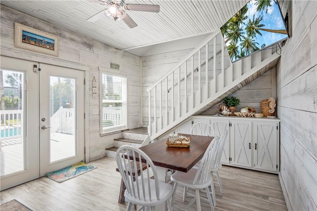 dining space featuring light wood-type flooring, wooden walls, ceiling fan, and stairs