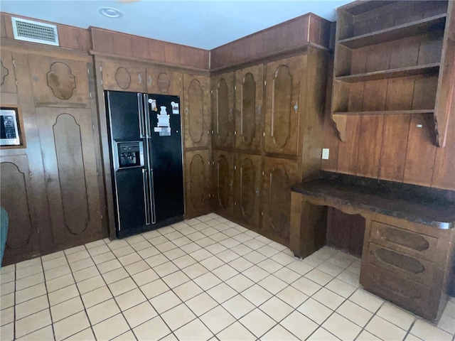 kitchen featuring wood walls, dark brown cabinetry, black refrigerator with ice dispenser, and light tile patterned floors