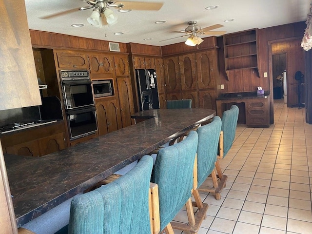 kitchen with black appliances, wood walls, light tile patterned flooring, and ceiling fan