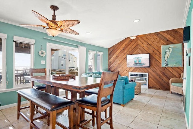 dining space featuring crown molding, ceiling fan, light tile patterned flooring, and wood walls