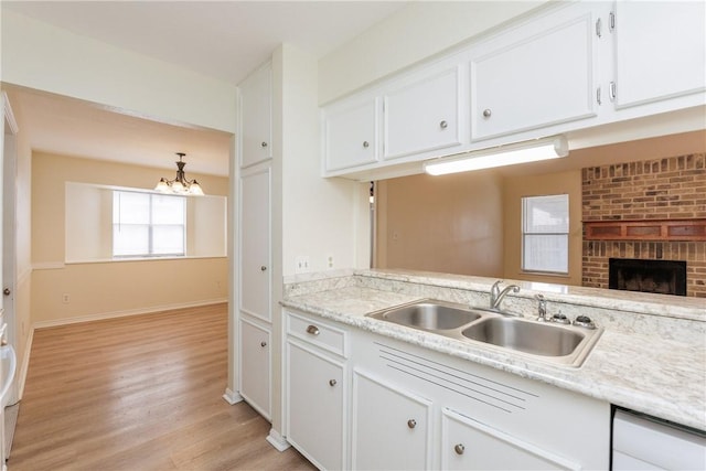 6117 Camwood Dr, Corpus Christi, TX 78415 - kitchen featuring a sink, a chandelier, white cabinets, light wood-style floors, and a brick fireplace