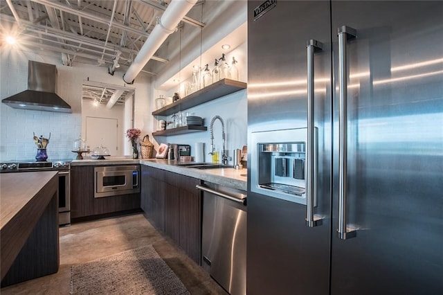 kitchen with sink, tasteful backsplash, wall chimney range hood, dark brown cabinets, and appliances with stainless steel finishes