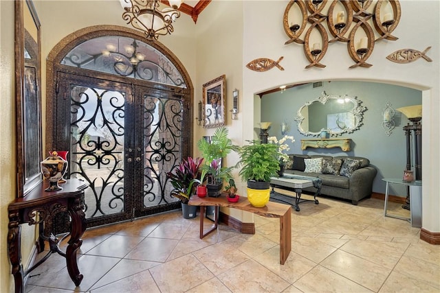 foyer entrance featuring crown molding, a high ceiling, a notable chandelier, light tile patterned flooring, and french doors