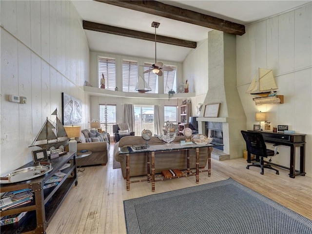 living room featuring a towering ceiling, beamed ceiling, a fireplace, ceiling fan, and light hardwood / wood-style flooring