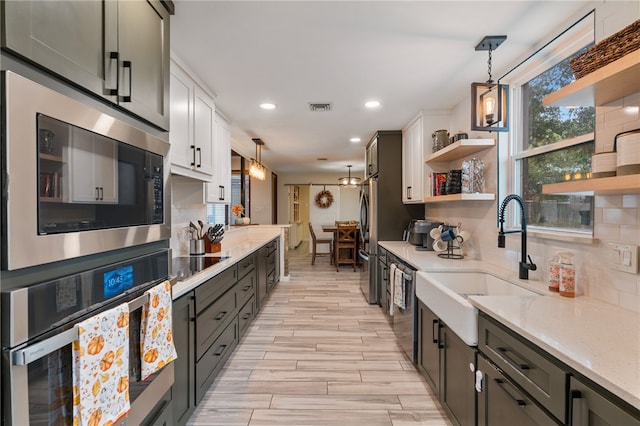 kitchen with hanging light fixtures, tasteful backsplash, white cabinetry, light wood-type flooring, and appliances with stainless steel finishes