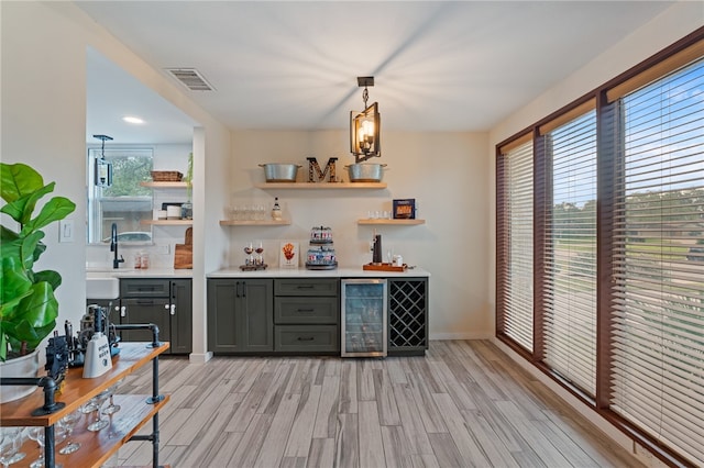 bar featuring gray cabinets, beverage cooler, hanging light fixtures, and light hardwood / wood-style flooring