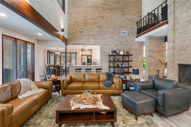 living room with hardwood / wood-style flooring, brick wall, beam ceiling, a towering ceiling, and a brick fireplace