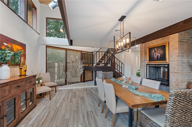 dining area featuring a brick fireplace, a high ceiling, a chandelier, and light hardwood / wood-style flooring