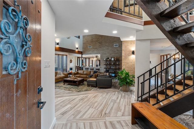 foyer featuring high vaulted ceiling, an inviting chandelier, light hardwood / wood-style floors, and brick wall