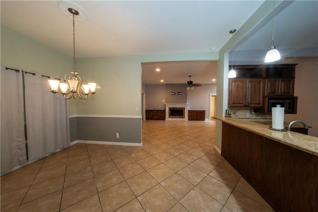 kitchen with pendant lighting, backsplash, ceiling fan with notable chandelier, light stone countertops, and light tile patterned flooring