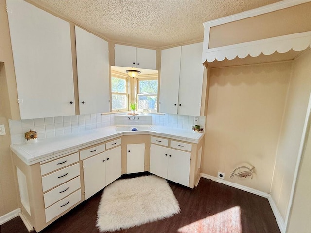 kitchen featuring dark wood-type flooring, backsplash, a sink, and white cabinetry