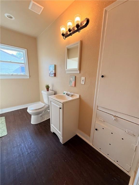 half bath featuring visible vents, toilet, vanity, wood finished floors, and baseboards