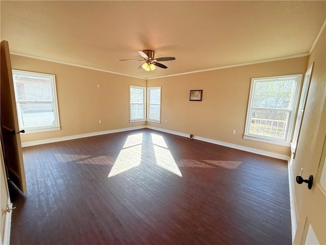 empty room with dark wood finished floors, a healthy amount of sunlight, crown molding, and baseboards