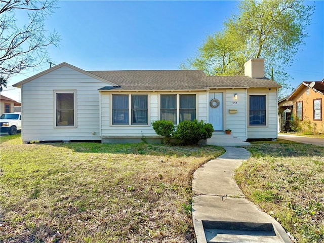 ranch-style house with roof with shingles, a chimney, and a front yard