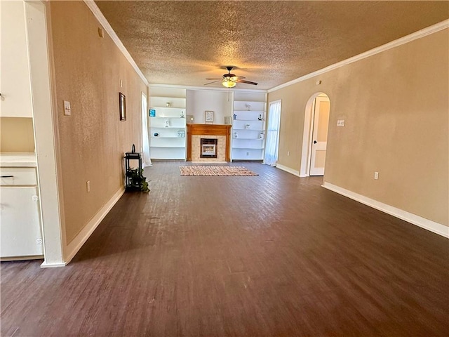 unfurnished living room with arched walkways, dark wood-style flooring, a fireplace, ornamental molding, and a textured ceiling