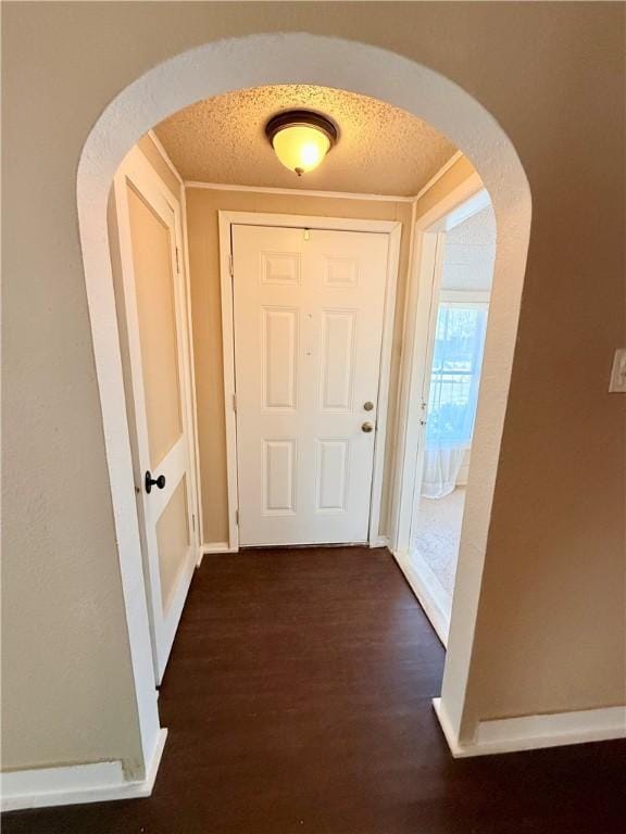 hall featuring arched walkways, dark wood-type flooring, a textured ceiling, and crown molding