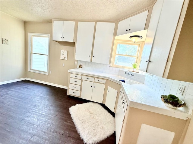 kitchen with dark wood-style flooring, tile countertops, tasteful backsplash, white cabinetry, and a sink