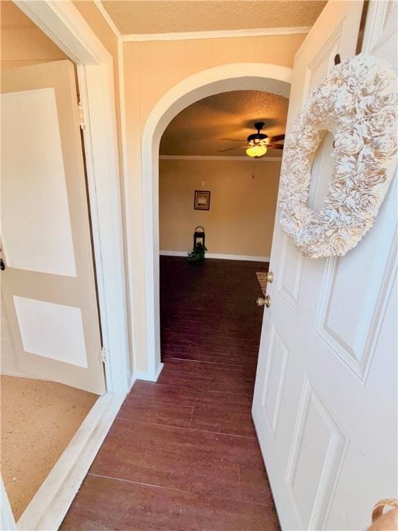 hallway featuring crown molding, arched walkways, dark wood finished floors, and baseboards