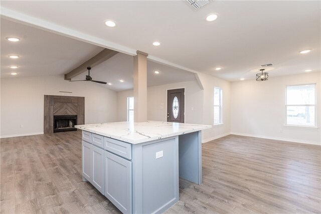 kitchen with light stone counters, light hardwood / wood-style floors, vaulted ceiling with beams, and a kitchen island