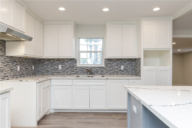 kitchen with sink, backsplash, light stone countertops, white cabinetry, and light wood-type flooring