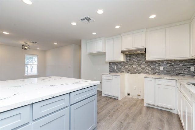 kitchen with white cabinetry, light wood-type flooring, decorative backsplash, and light stone countertops