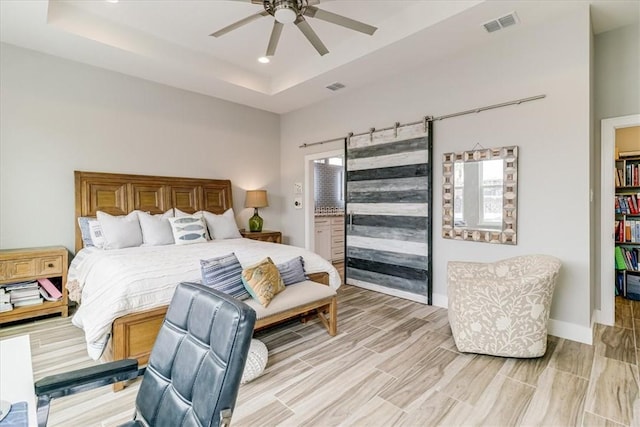 bedroom with a raised ceiling, ceiling fan, visible vents, and light wood-style floors