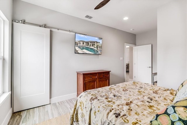 bedroom featuring light wood finished floors, a barn door, a ceiling fan, visible vents, and baseboards
