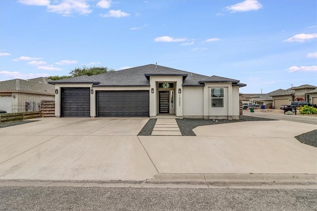 prairie-style home featuring stucco siding, fence, roof with shingles, concrete driveway, and an attached garage