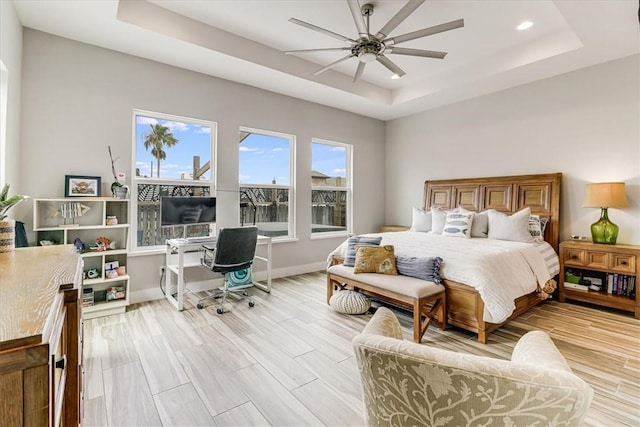 bedroom featuring recessed lighting, light wood-style floors, ceiling fan, a tray ceiling, and baseboards