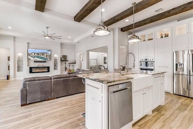 kitchen featuring a kitchen island with sink, light stone counters, stainless steel appliances, ceiling fan, and a sink