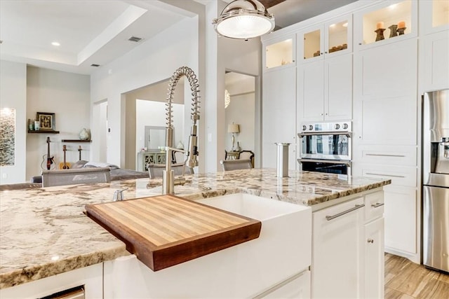 kitchen with glass insert cabinets, light stone countertops, white cabinets, and appliances with stainless steel finishes