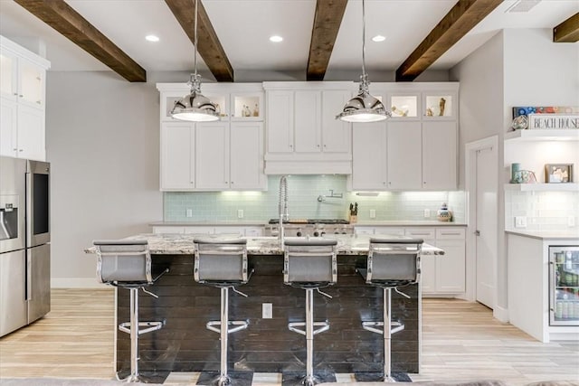 kitchen with light wood-type flooring, a center island with sink, beamed ceiling, and backsplash