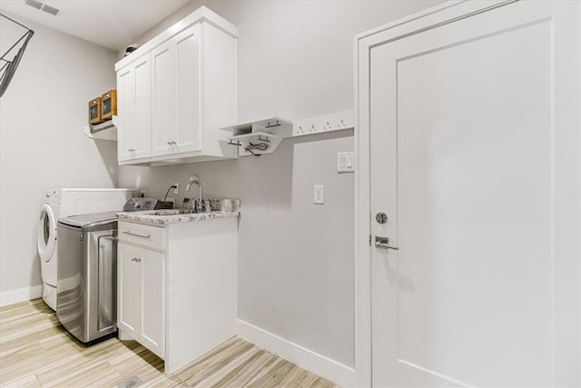laundry room with light wood-type flooring, washing machine and clothes dryer, cabinet space, and baseboards