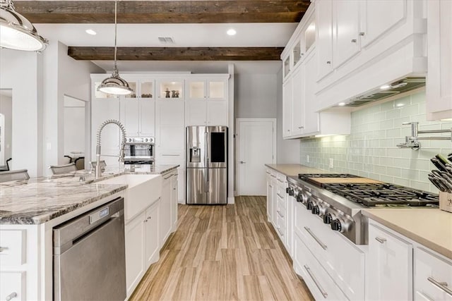 kitchen featuring white cabinetry, beamed ceiling, a sink, stainless steel appliances, and light wood finished floors