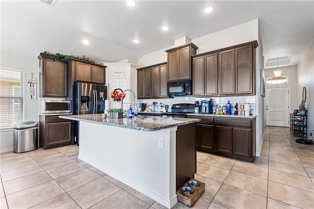 kitchen featuring lofted ceiling, black appliances, a kitchen island with sink, light tile patterned flooring, and stone countertops