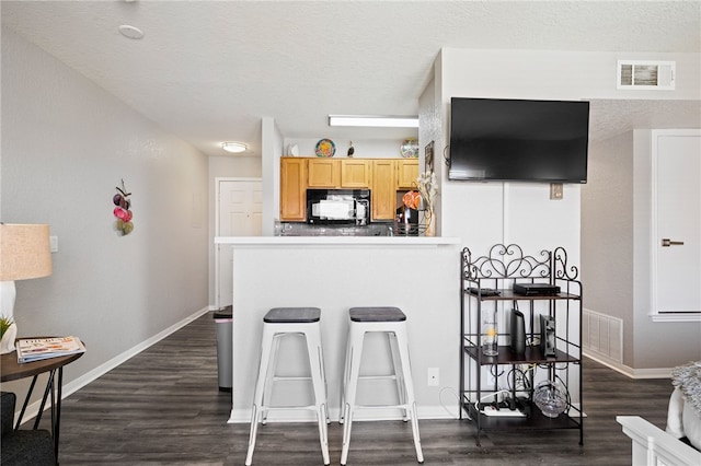 kitchen featuring light brown cabinets, a kitchen breakfast bar, dark hardwood / wood-style flooring, and a textured ceiling