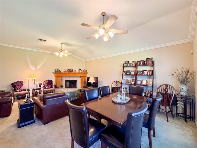 carpeted dining space featuring a tiled fireplace, lofted ceiling, ceiling fan, and crown molding