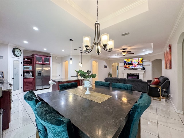 dining room with light tile patterned flooring, ceiling fan with notable chandelier, ornamental molding, and a tray ceiling