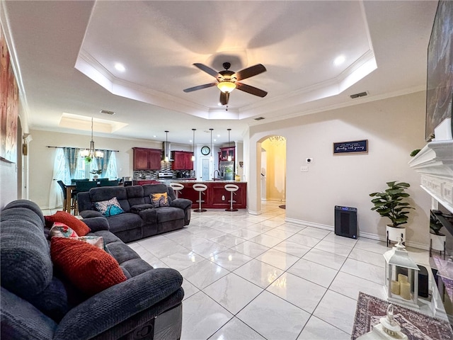 living room with sink, a tray ceiling, ceiling fan with notable chandelier, and crown molding