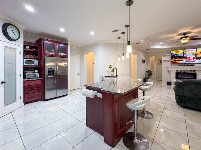 kitchen with a center island with sink, a breakfast bar, ceiling fan, decorative light fixtures, and stainless steel fridge