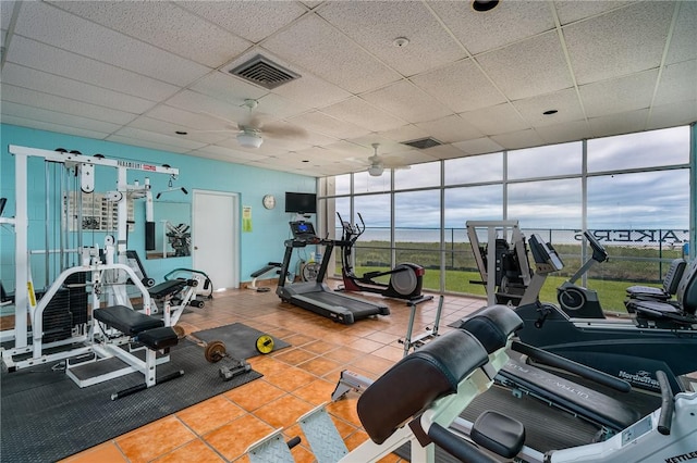 exercise room with a wall of windows, visible vents, ceiling fan, and a drop ceiling