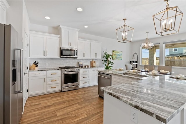 kitchen featuring white cabinetry, hanging light fixtures, stainless steel appliances, and an island with sink