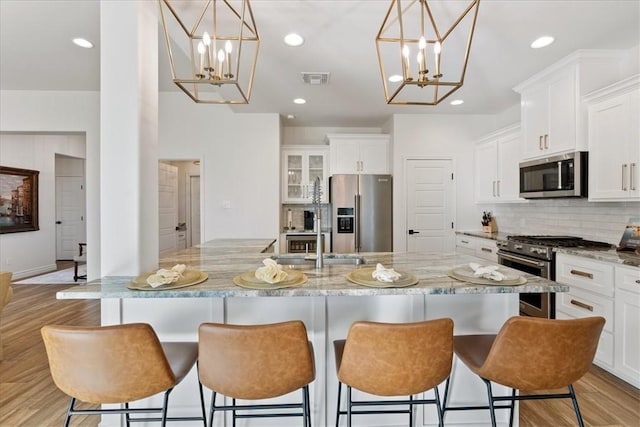 kitchen with white cabinetry, high quality appliances, hanging light fixtures, and a center island with sink