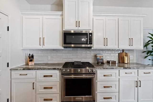 kitchen with backsplash, stainless steel appliances, dark stone countertops, and white cabinets