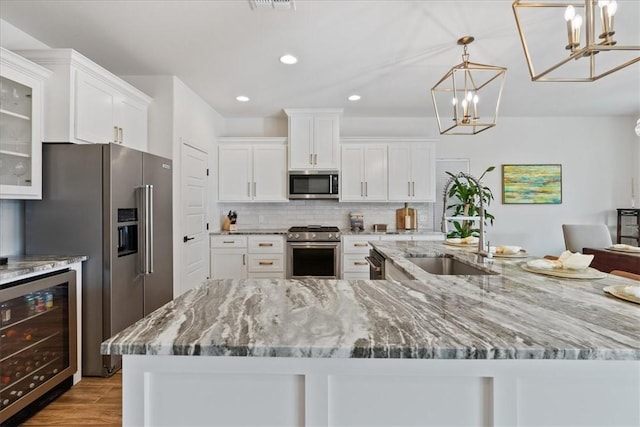 kitchen with appliances with stainless steel finishes, pendant lighting, white cabinets, beverage cooler, and backsplash